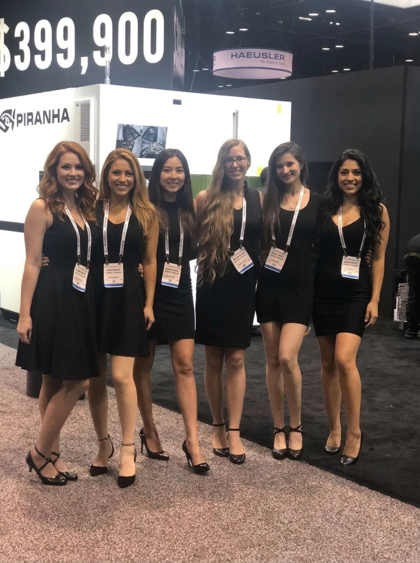 Six trade show models in matching black cocktail dresses and show lanyards at an industrial machinery booth, the kind of crew Purple sends to Kansas City shows
