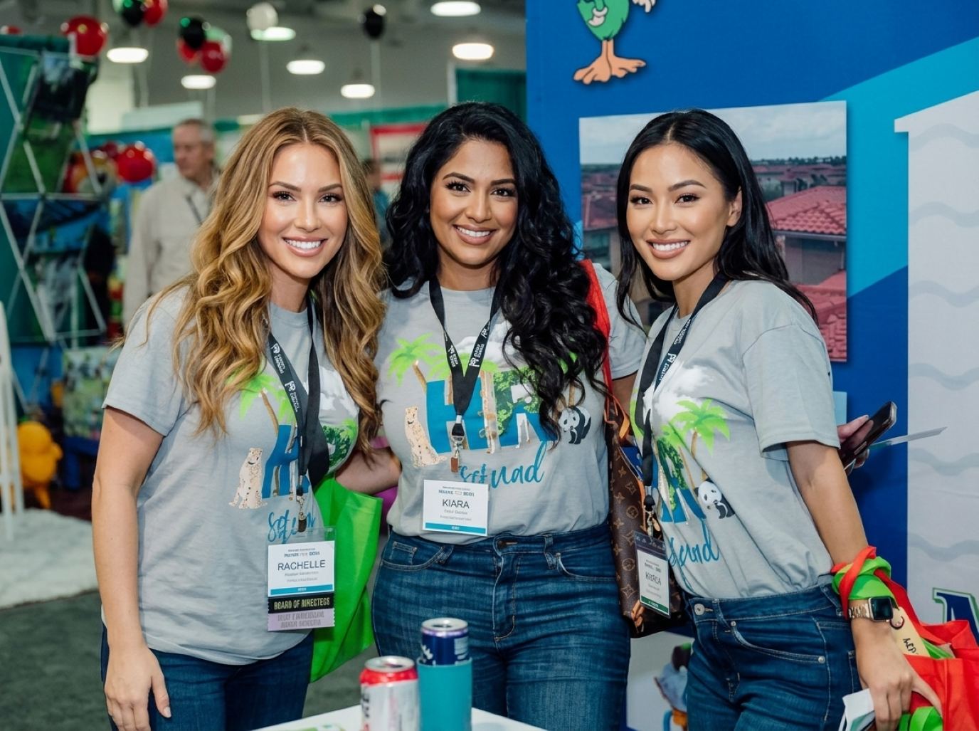 Three brand ambassadors in matching gray logo tees, jeans and lanyards smiling at an exhibit booth, the kind of trade show models Purple books for PGA Show exhibitors