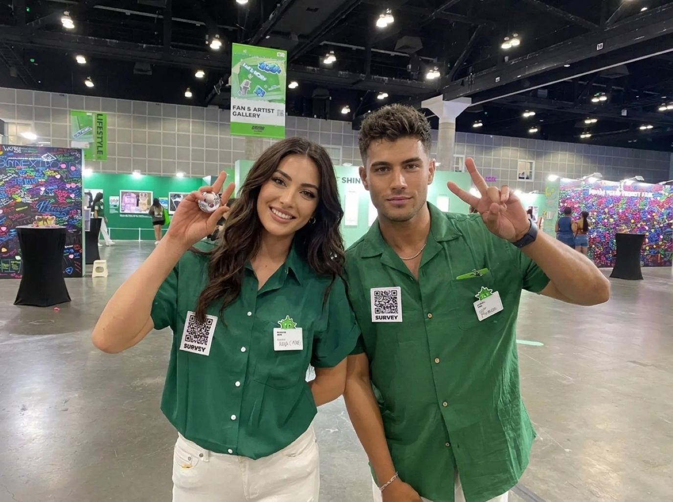 Two hosts in matching green camp shirts and white jeans with QR survey badges, the polished look of PGA Show booth staff from Purple Exhibits
